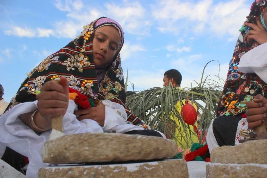 Girl wearing the traditional dress of Siwa grinding salt
