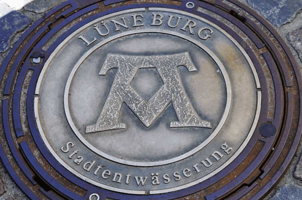 Manhole cover displaying the symbol for the motto "Mons, Pons, Fons"