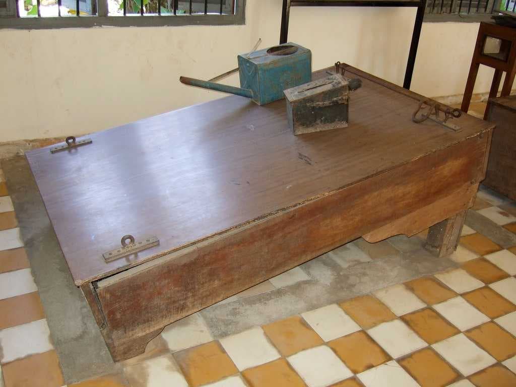 Waterboard displayed at Tuol Sleng. Prisoners' legs were shackled to the bar on the right, their wrists were restrained to the brackets on the left and hot water was poured over their face using the blue watering can.