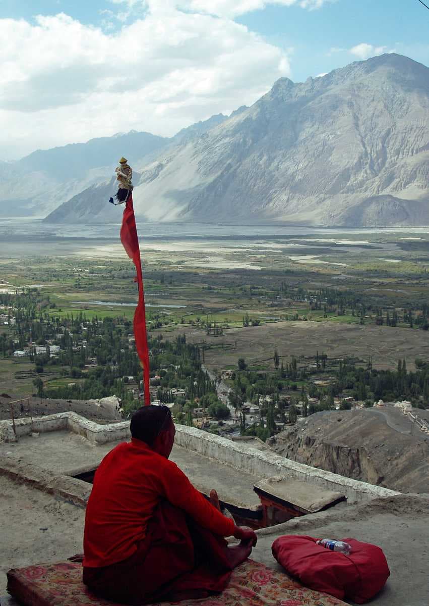 A monk meditates on terrace of Diskit monastery, with Nubra Valley and Diskit village seen in the background